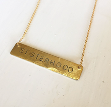 Load image into Gallery viewer, A bar necklace with the word SISTERHOOD  stamped into the brass. It hangs on a gold plated chain 16 inches long.