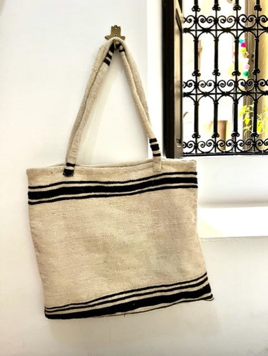 A large and spacious Moroccan carpet tote bag. Handmade it is one of a kind. Predominantly neutral it features a horizontal dark brown stripe. 