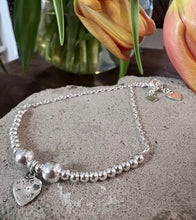 Load image into Gallery viewer, sterling silver beaded bracelet has a central heart charm and two larger beads either side of it. These beads are on a chain  bracelet and each end is finished with a small flat heart.