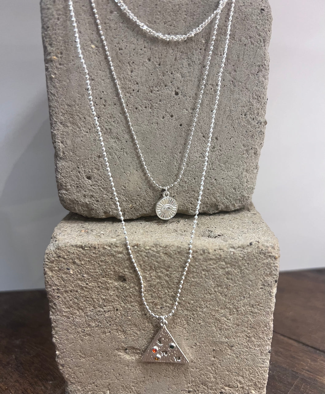 triple layered silver plated necklace with a triangular pendant with moon and stars and a circular one with the evil eye within sun rays