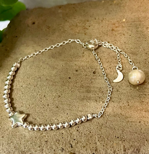 A sterling silver beaded  bracelet with a star  and a moon and pearl at the ends of the chain