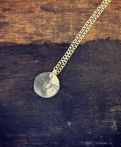 A sterling silver disc necklace with a pretty heart and radiating  dots emerging from it on a sterling silver chain.