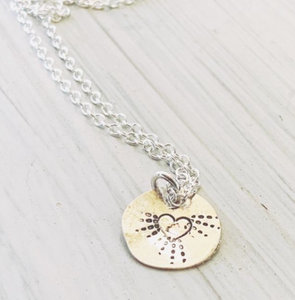 A sterling silver disc necklace with a pretty heart and radiating  dots emerging from it on a sterling silver chain.