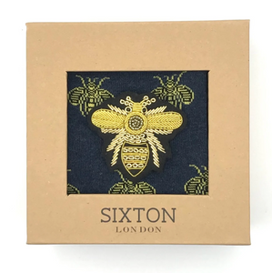 A pair of navy blue socks with yellow bee designs on them and a large bee pin. All presented in a box.