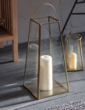 Load image into Gallery viewer, A large brass lantern. Delicate brass structure with glass sides. A moving handle to the top so it can be placed up or down. A flat base in brass to stand a pillar candle on. THe underneath has a black felt base so it can be stood on a table or on a fireplace hearth. 