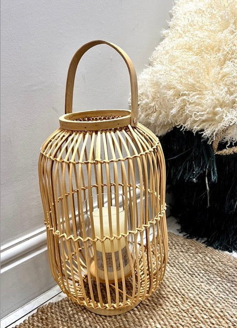A large natural lantern made from rattan with a metal stand and glass surround for the candle