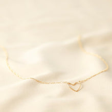 Load image into Gallery viewer, A 14ct gold plated brass necklace. The pendant to the front is shaped as the outline of a heart. It is attached either side to a figaro style chain. With a soft sheen. Lobster clasp and extender chain to the back.