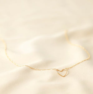A 14ct gold plated brass necklace. The pendant to the front is shaped as the outline of a heart. It is attached either side to a figaro style chain. With a soft sheen. Lobster clasp and extender chain to the back.