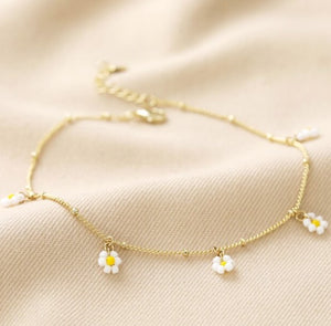 Made from 14ct gold plated brass, it features white and yellow bead daisy charms which dangle from the chain. The chain is a satellite style with a lobster clasp and a 3cm extender chain for adjustable wearing.