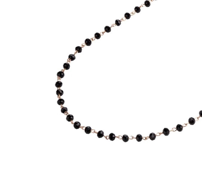 A long beaded necklace in black on a gold chain. 