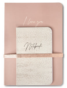 A set of two notebooks in different sizes. The large is in a dusty antique rose with a metallic rose gold elastic band holding the second in place. The large book has the words I LOVE YOU written on it in gold. The small book is a soft green with gold spatters on it and the word NOTEBOOK on it. A lovely gifting set  for someone you love