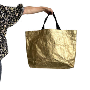 A giant gold sturdy shopper made from 100% recycled paper and woven fabric straps in black.